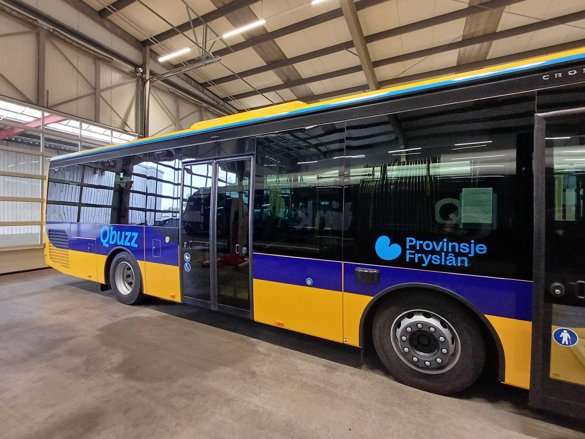 Een blauw-gele Qbuzz bus met het logo van Provincie Fryslân geparkeerd in een garage.