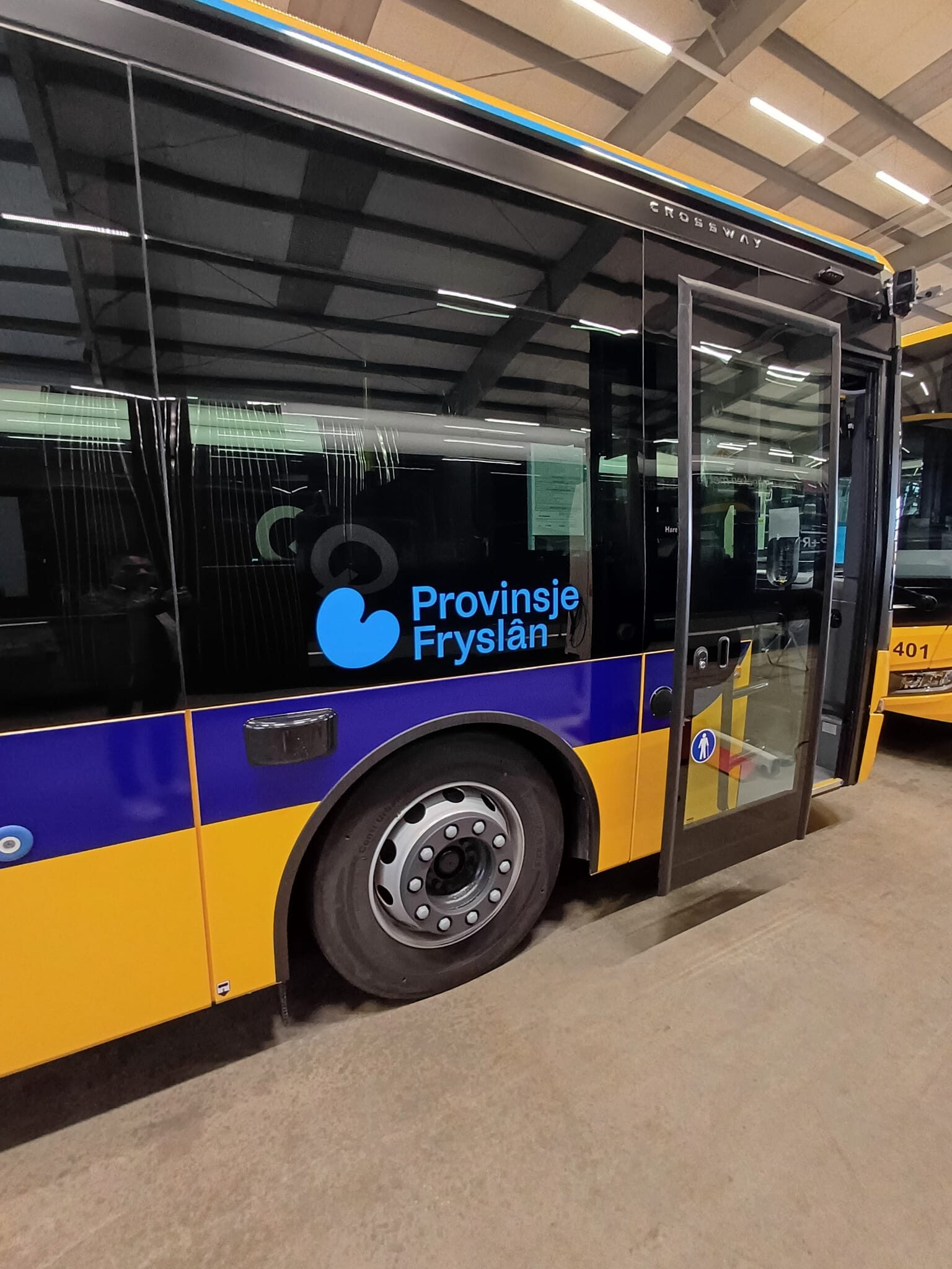 Een gele lijnbus met het logo van de Provincie Fryslân staat geparkeerd in een overdekte ruimte.