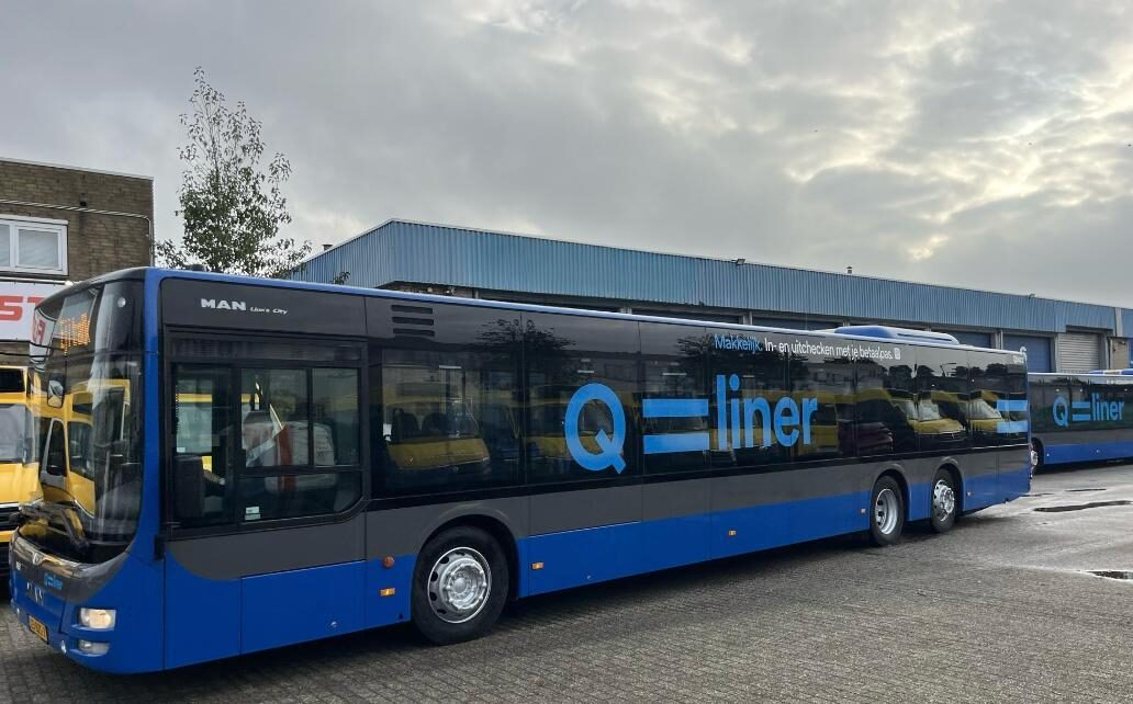 Een blauwe en zwarte Q-liner bus geparkeerd op een bedrijventerrein.