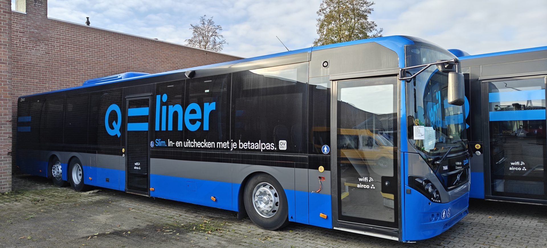 Een blauwe Q-liner bus geparkeerd naast een bakstenen muur.