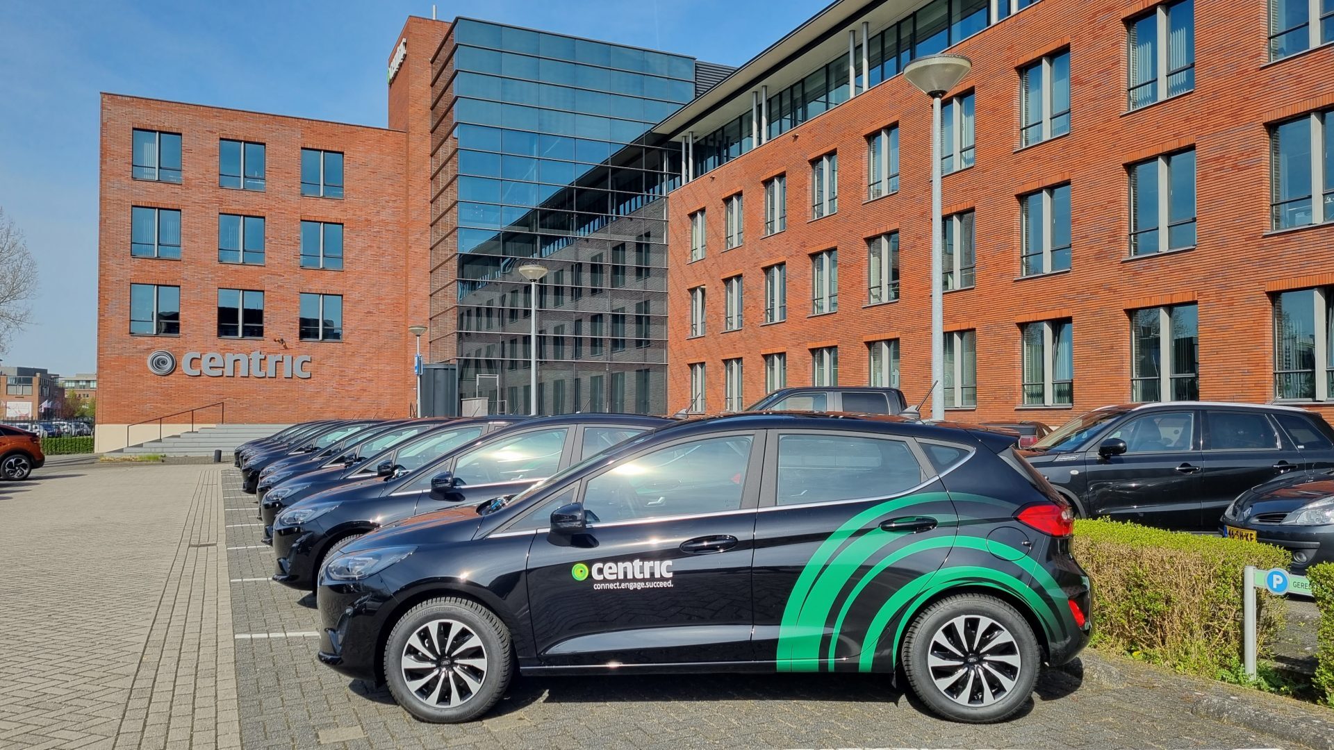 Parkeerplaats met auto's van Centric voor een modern kantoorpand.