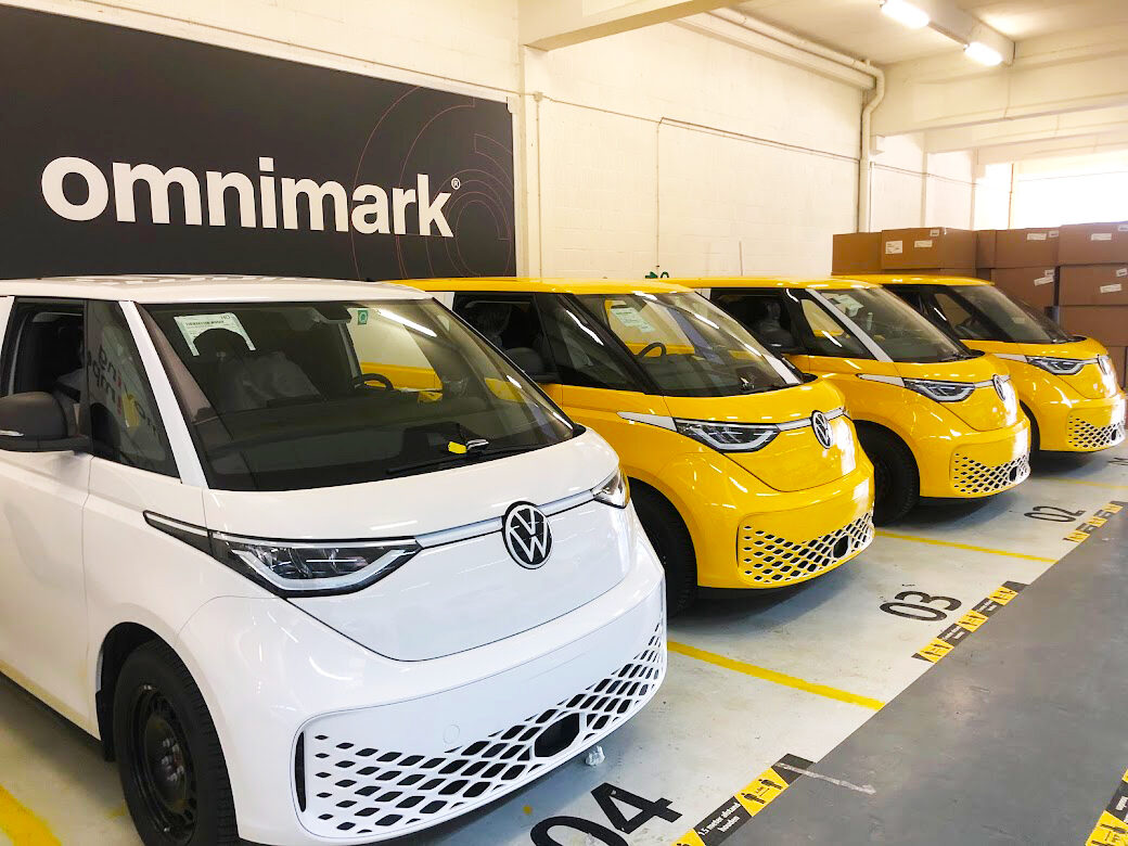Vier Volkswagen ID. Buzz voertuigen in een garage, één wit en drie geel geparkeerd bij Omnimark.