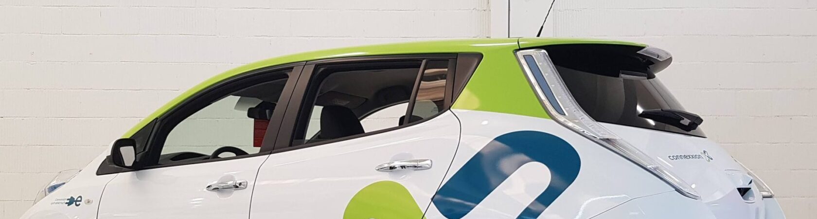 Een witte elektrische auto van Connexxion met groene en blauwe accenten geparkeerd in een lichte ruimte.
