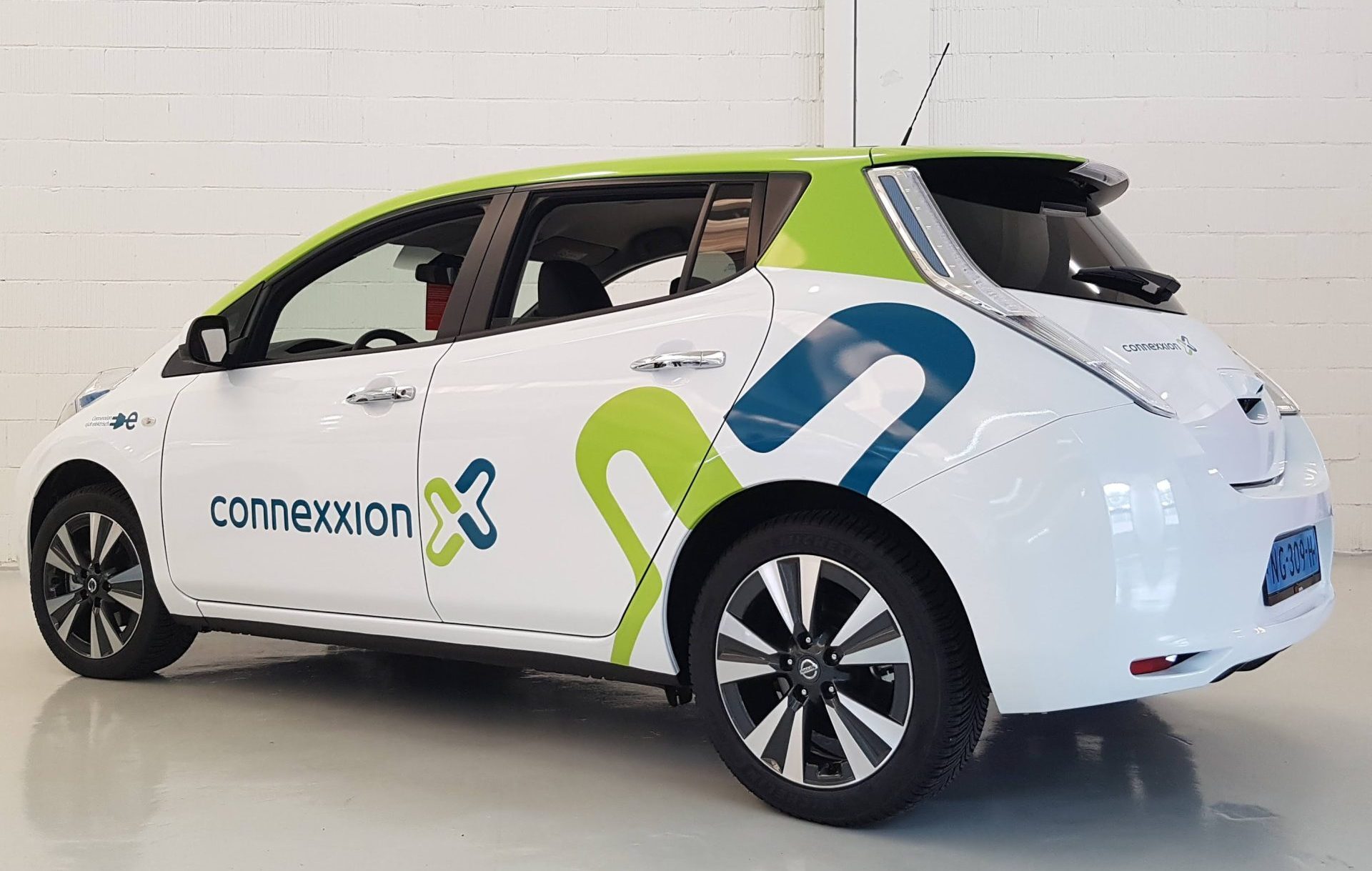 Een witte elektrische auto van Connexxion met groene en blauwe accenten geparkeerd in een lichte ruimte.