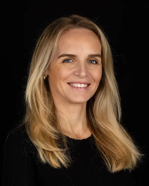 Portretfoto van een lachende vrouw met blond haar en een zwarte achtergrond.