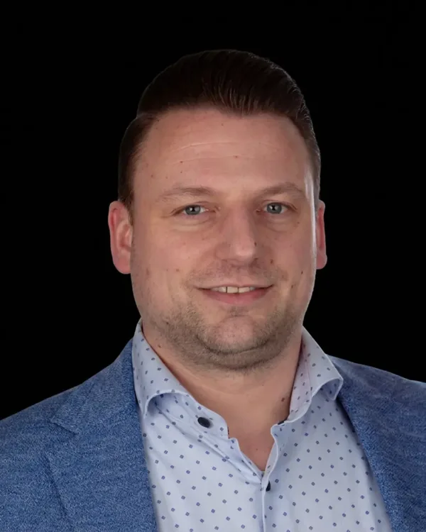 Portret van een man in een blauw jasje en gestippeld overhemd op een zwarte achtergrond.