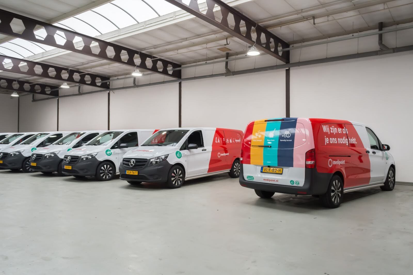 Verschillende Medux-bestelwagens met kleurrijke belettering staan geparkeerd in een loods.