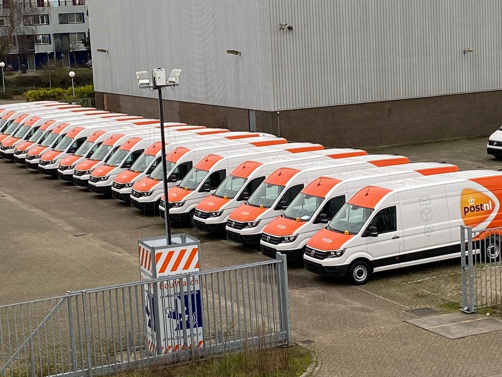 Een rij PostNL-bestelwagens geparkeerd op een industrieterrein.
