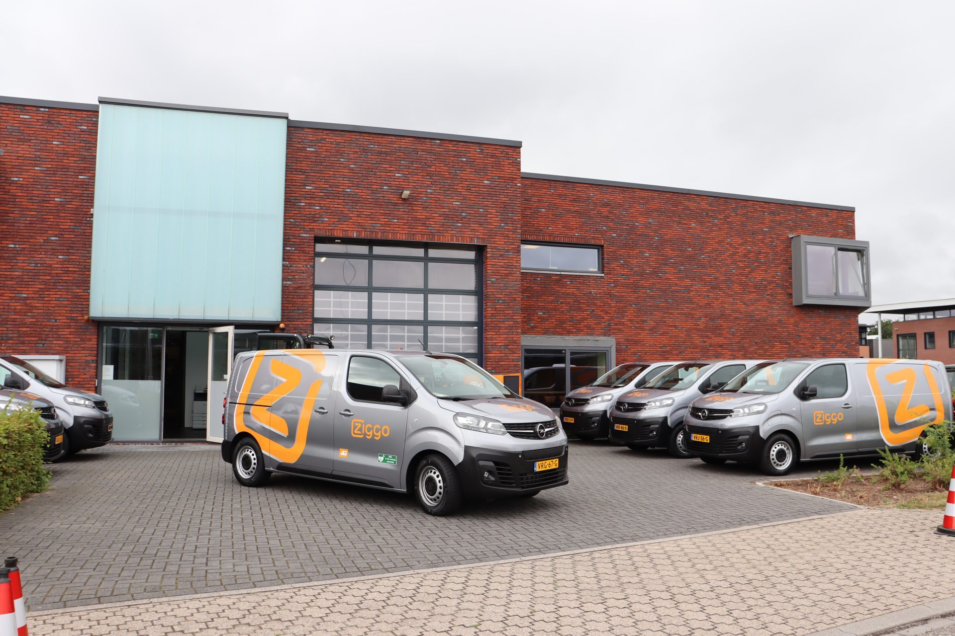 Zes Ziggo-bestelwagens geparkeerd voor een modern bakstenen gebouw op een bedrijventerrein.