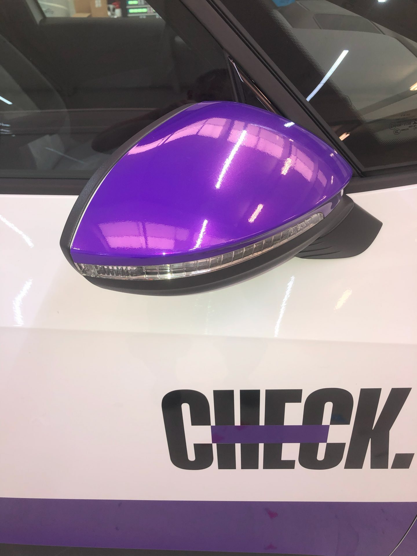 De afbeelding toont een paarse autospiegel op een witte auto met het woord 