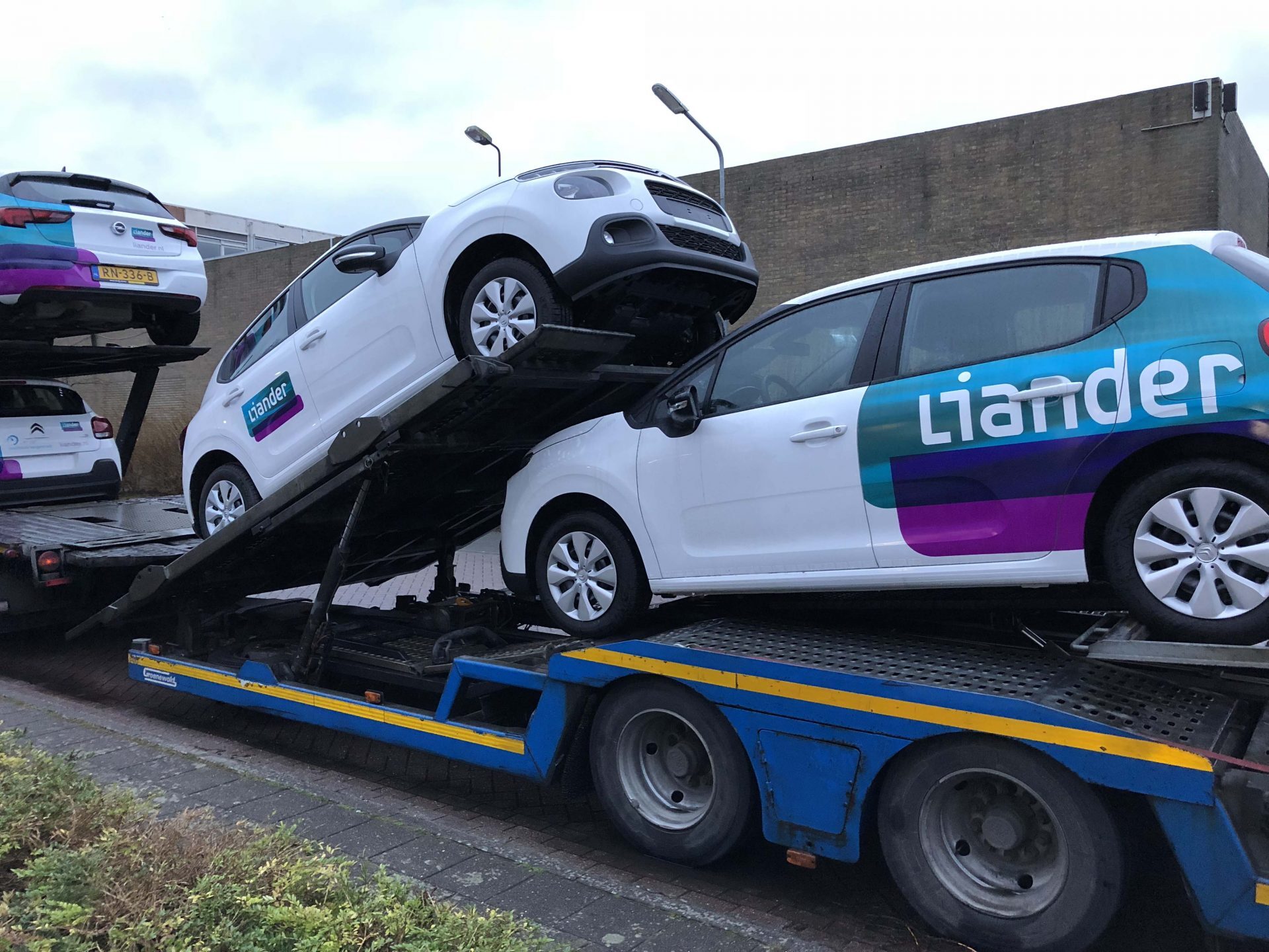 Witte Liander-auto's staan op een blauwe autotransporter geparkeerd.