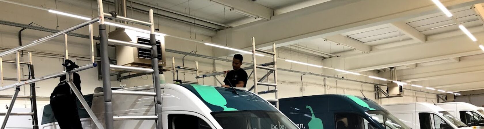 Werknemers zijn bezig met het beplakken van bestelwagens in een werkplaats.