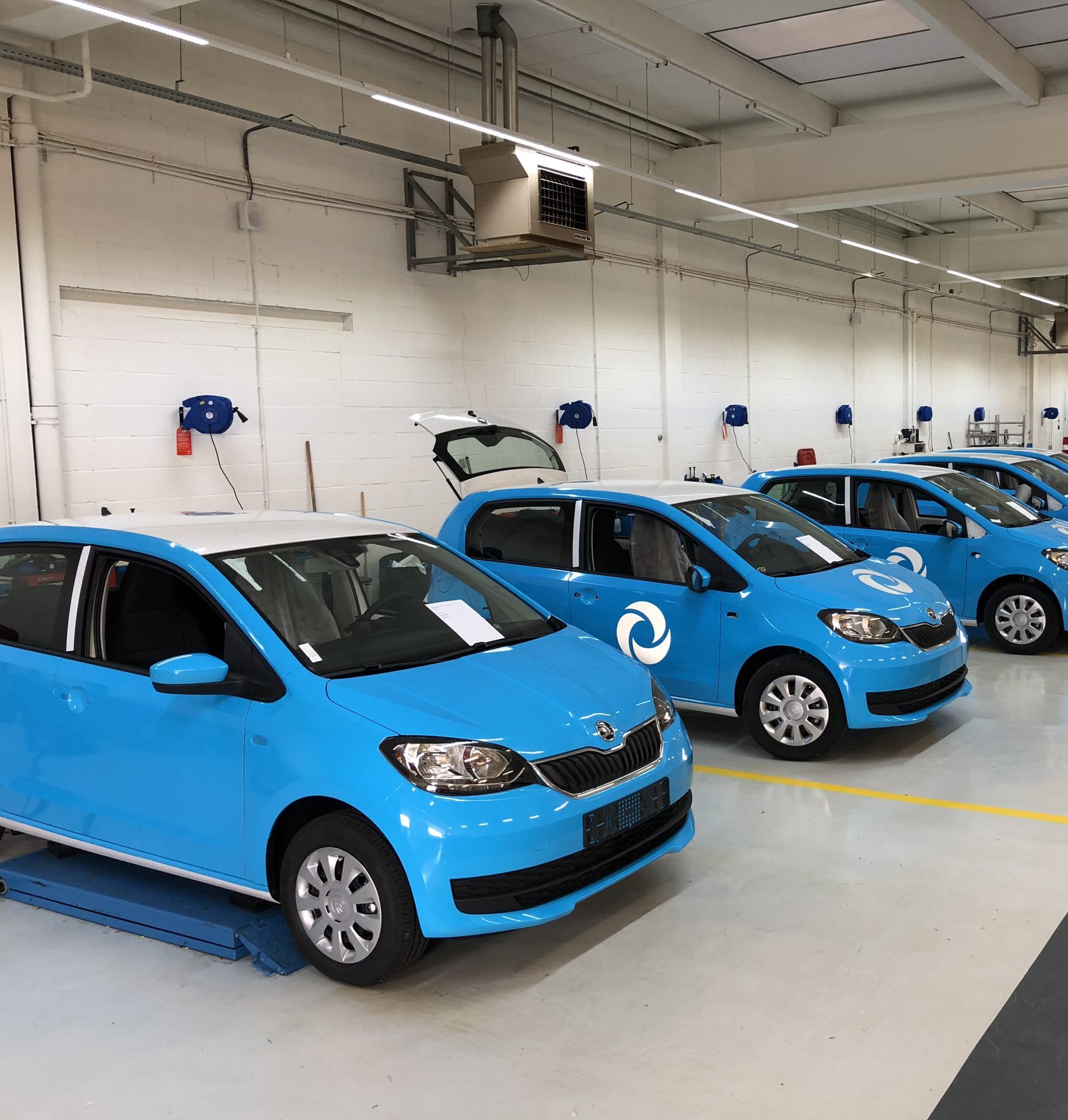 Een rij blauwe auto's met een logo, geparkeerd in een werkplaats.