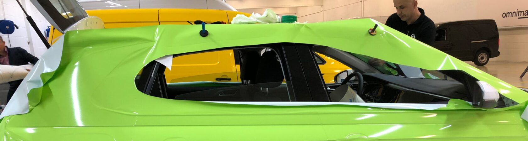 Een medewerker van Omnimark brengt een groene vinylfolie aan op een auto in een werkplaats.