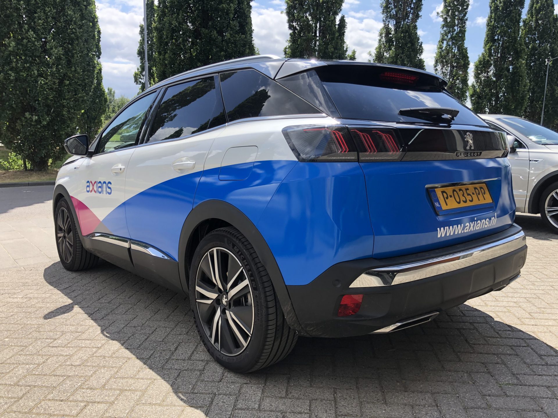 Een Peugeot auto van Axians met blauw-witte bestickering geparkeerd op een zonnige dag.
