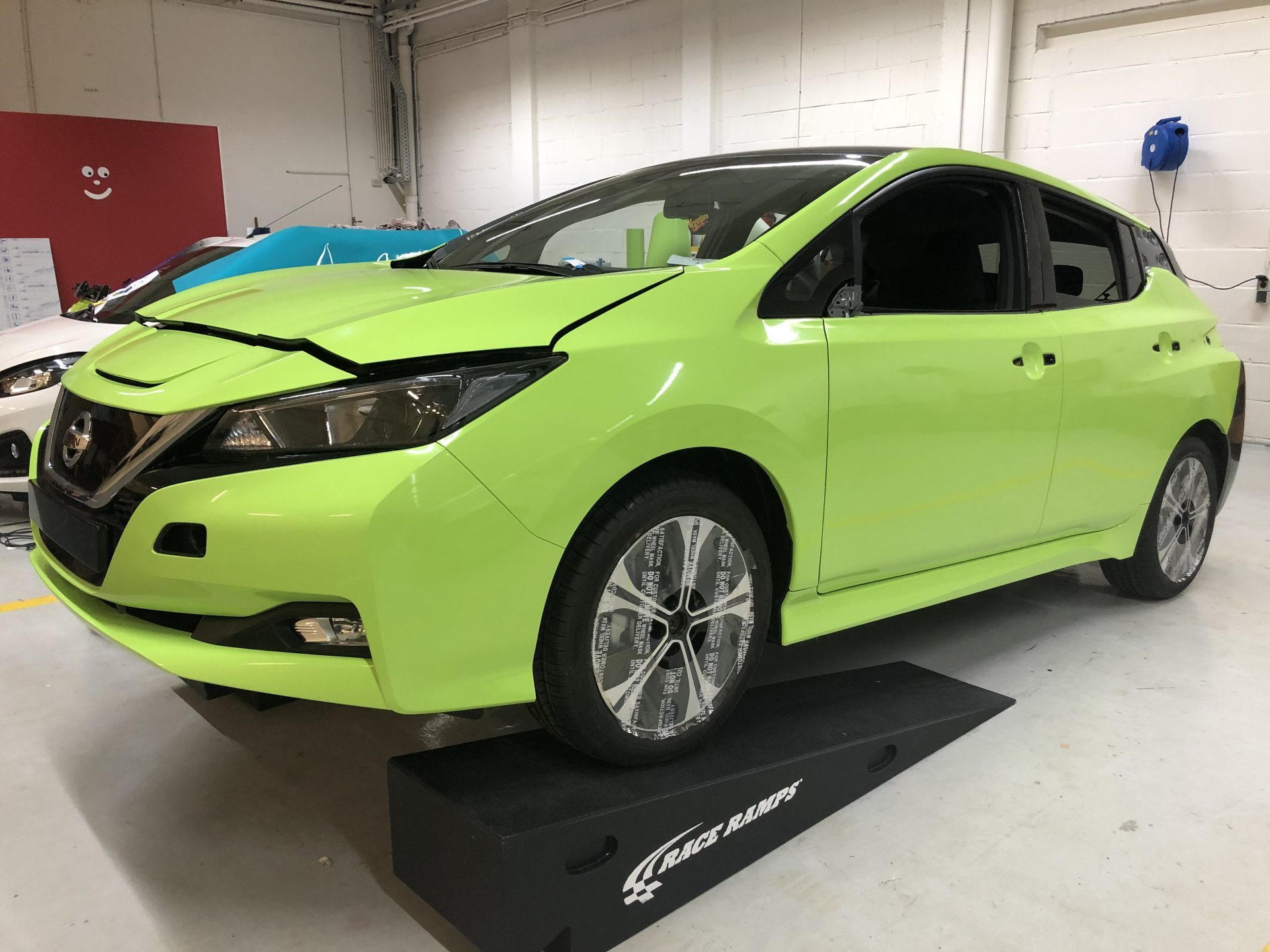 Een felgroene auto staat geparkeerd op een set ramps in een garage.
