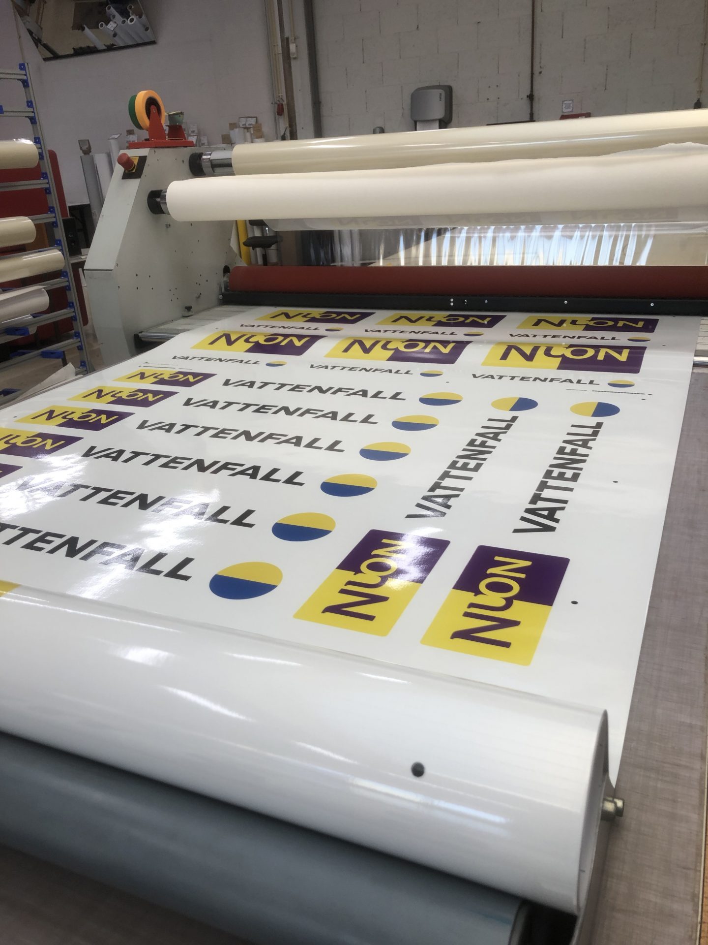 Een lamineermachine is bezig met het verwerken van vellen met het logo van Nuon en Vattenfall.