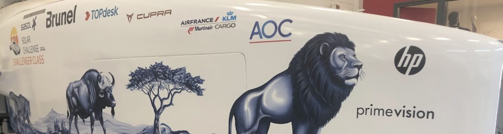 Een close-up van een voertuig met sponsorlogo's en afbeeldingen van een leeuw en een gnoe op de zijkant.