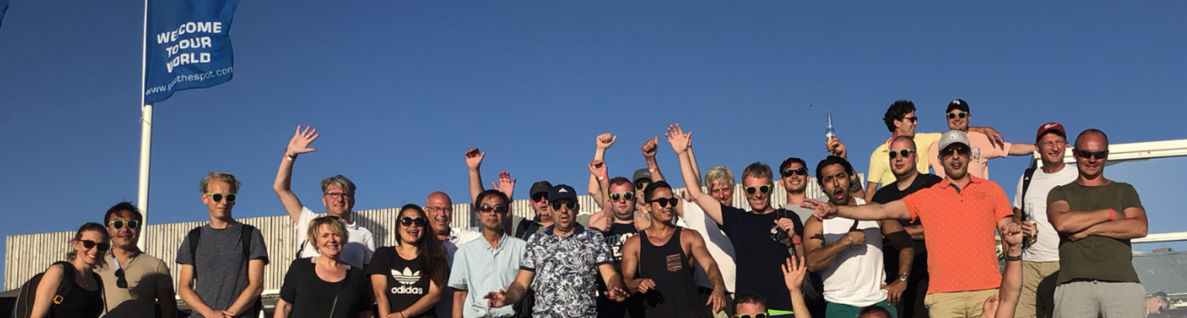 Groep mensen poseert vrolijk voor een foto op het strand onder een blauwe hemel.