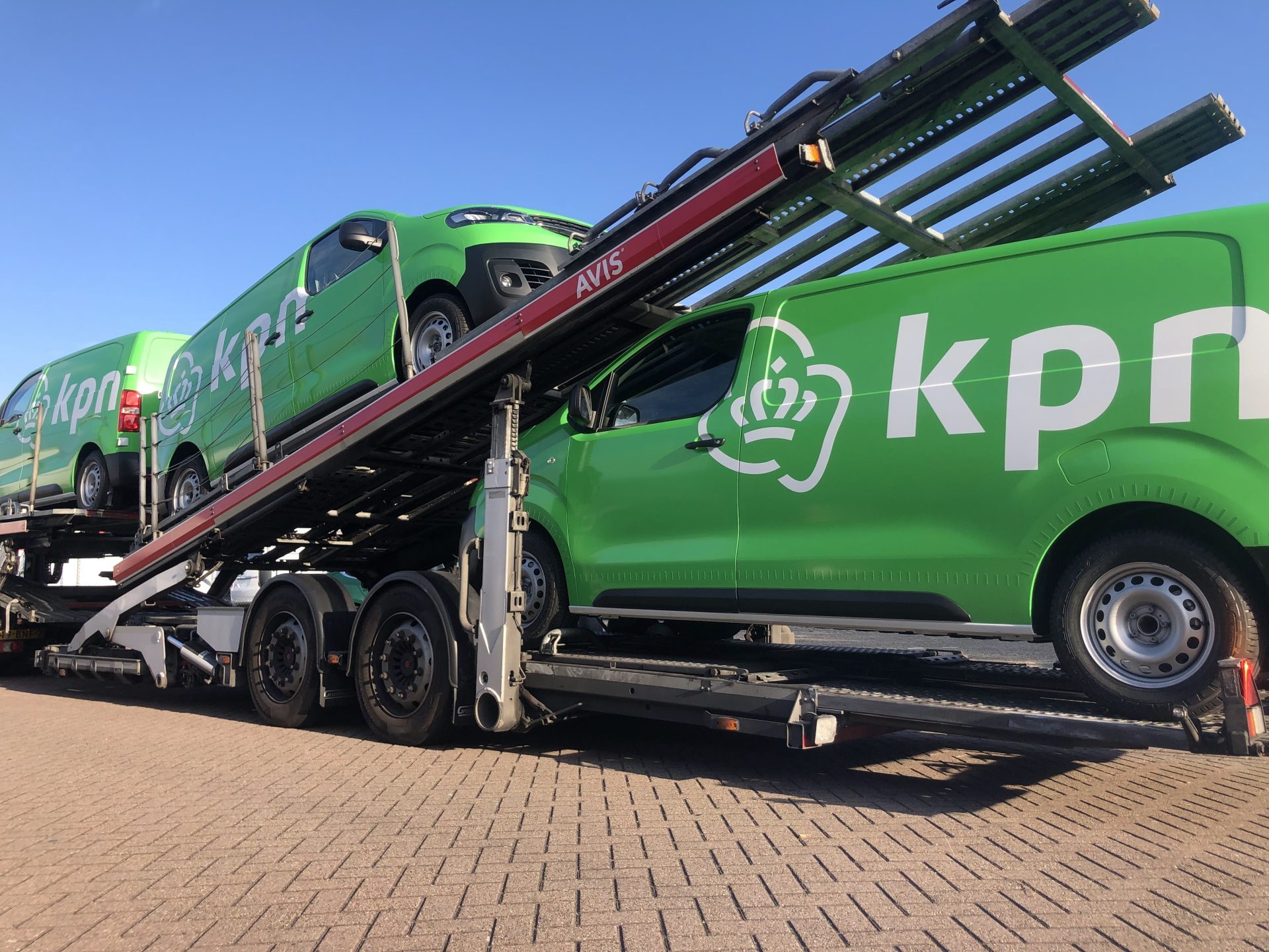 Groene KPN-bestelwagens op een autotransporteur tegen een heldere blauwe lucht.