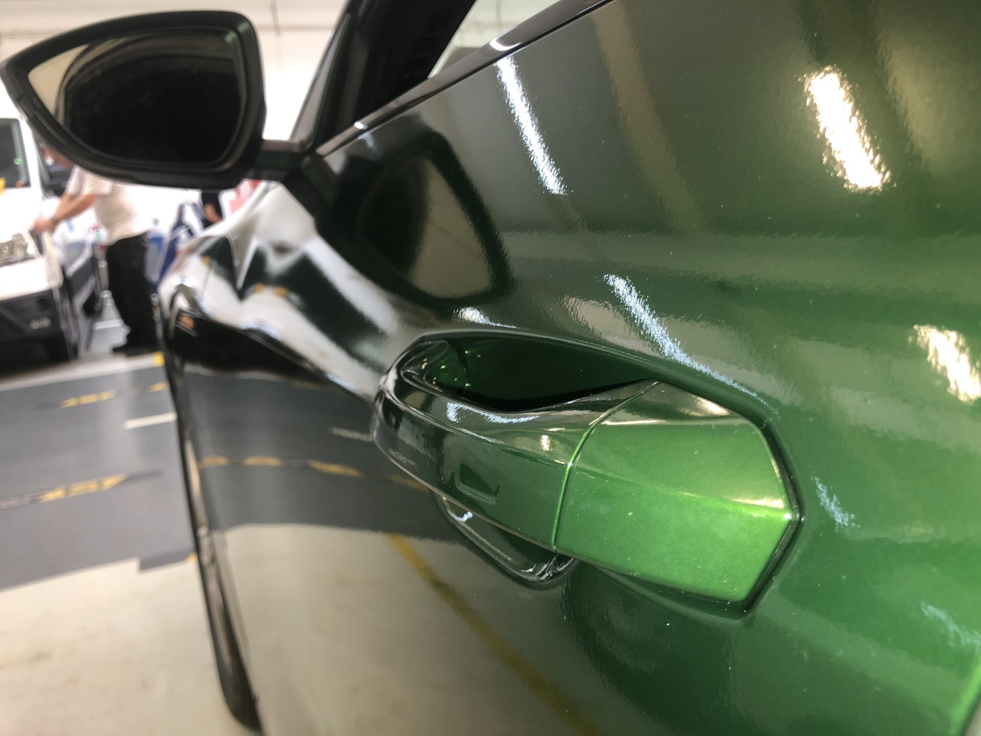 Close-up van de zijkant van een glanzende groene auto met deurgreep.