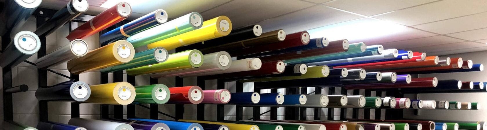 Een wand met kleurrijke rollen folie in een opslagruimte.