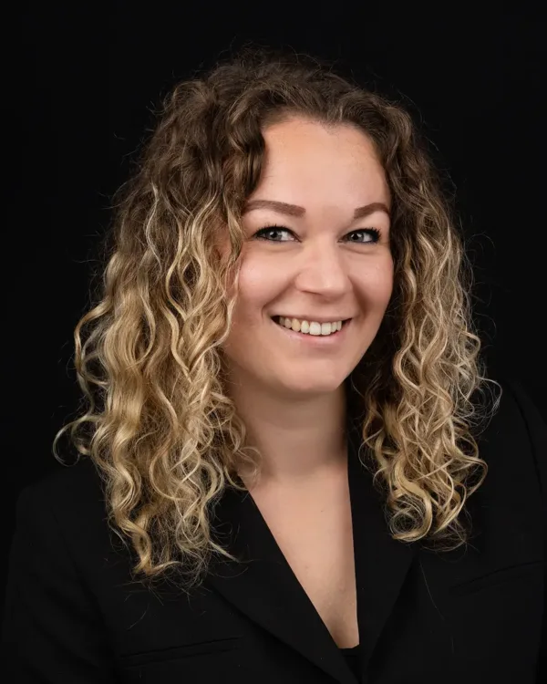 Portret van een lachende vrouw met krullend haar tegen een donkere achtergrond.