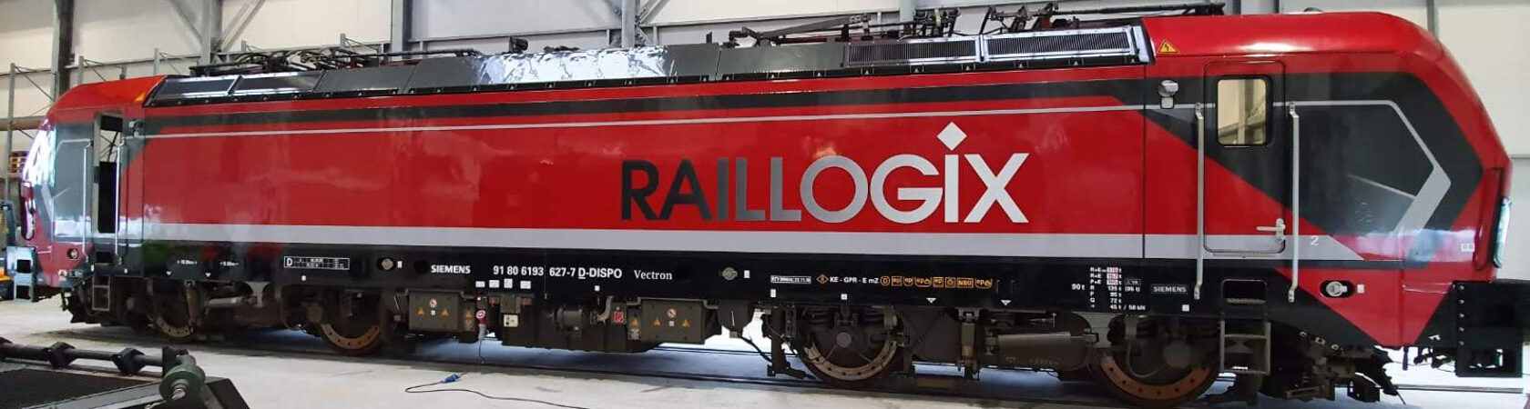 Rode locomotief met het Raillogix logo in een werkplaats.