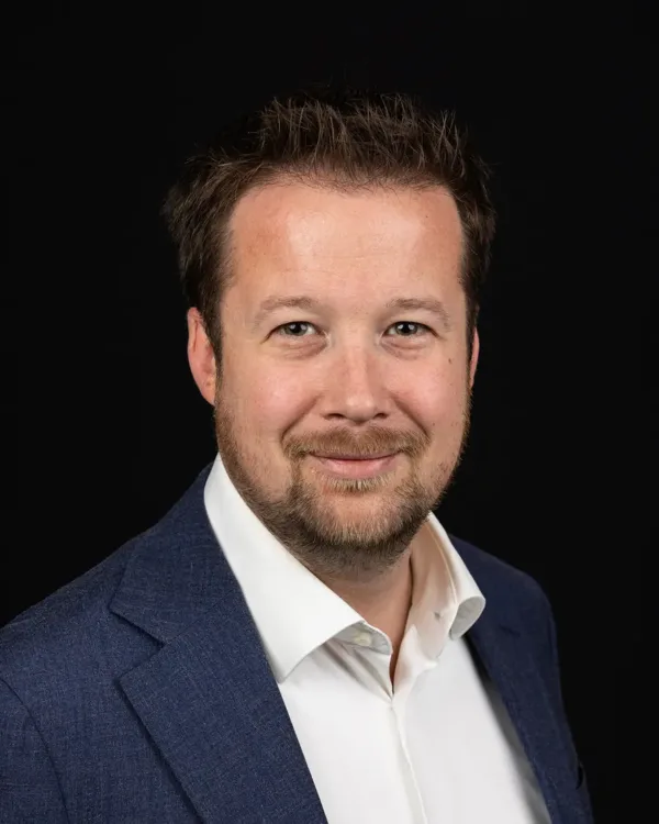 Portret van een man in een blauw pak met een witte overhemd, lachend naar de camera.