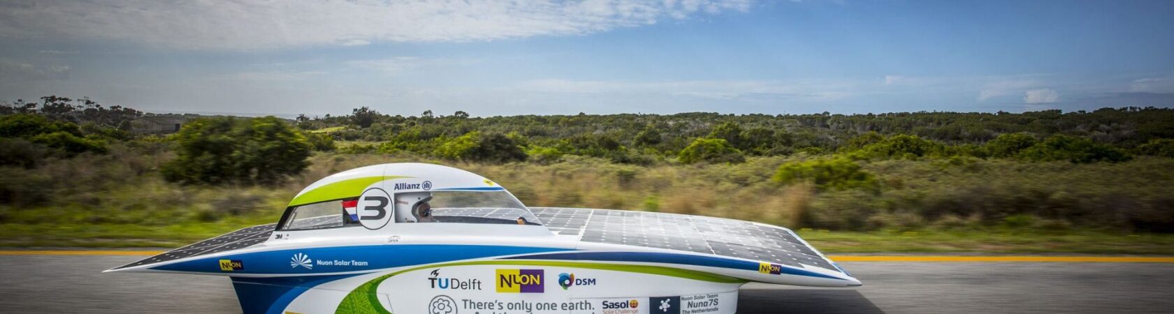 De Nuna7S zonneauto van het Nuon Solar Team rijdt op een weg met een groene achtergrond.