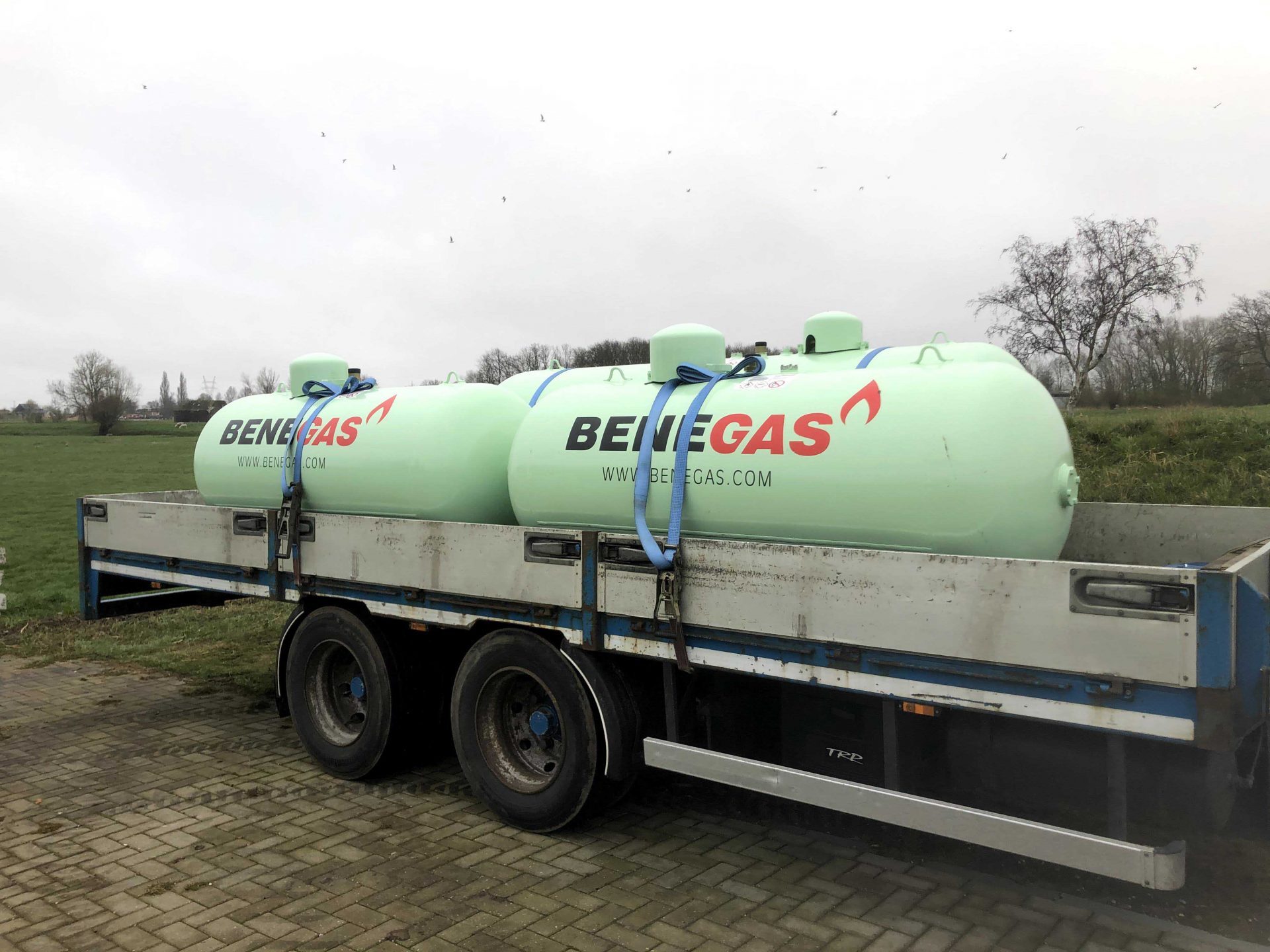 Twee grote Benegas gastanks zijn vastgebonden op een aanhanger naast een grasveld.