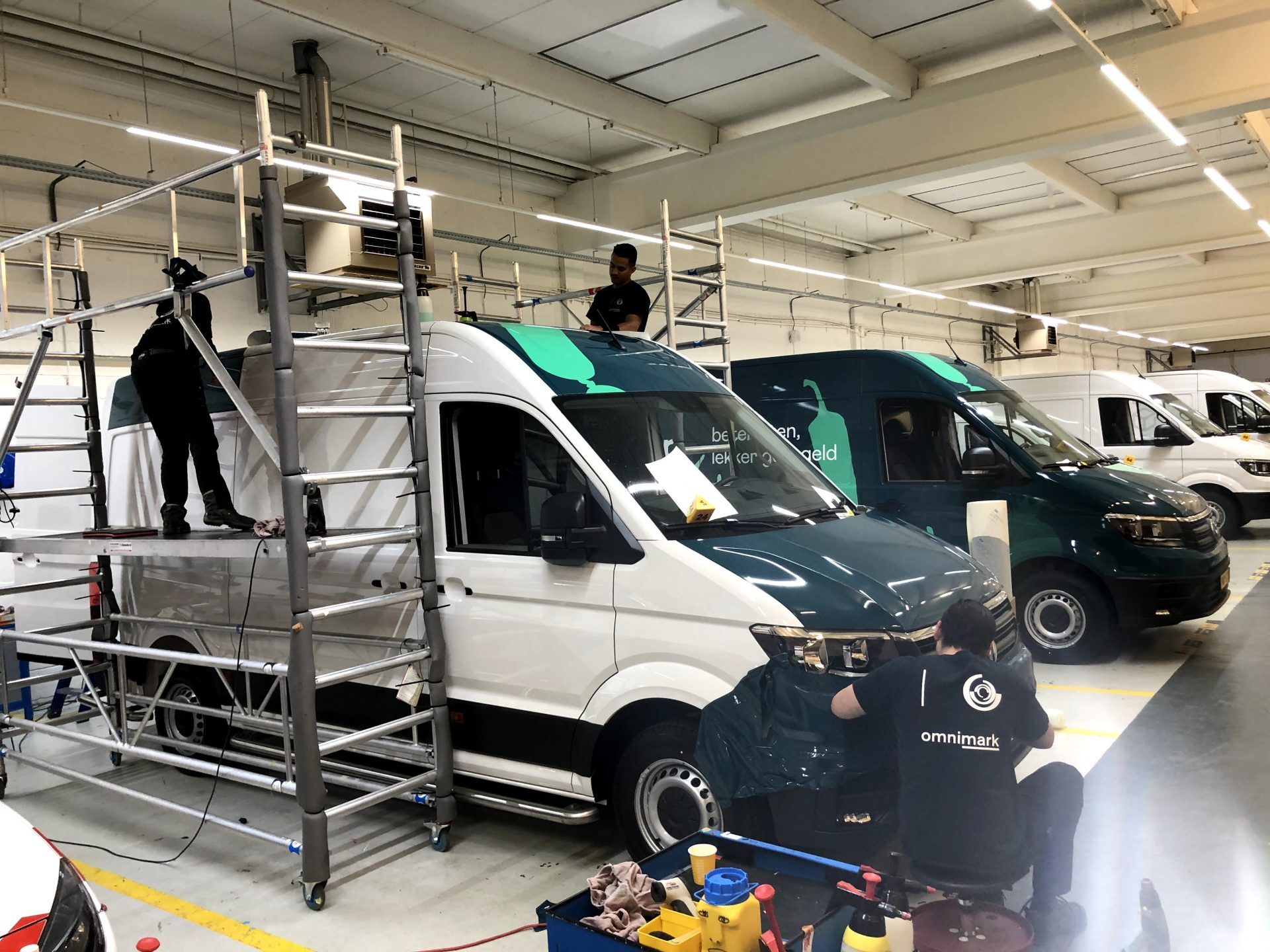 Mensen werken aan het beletteren en bestickeren van bestelwagens in een werkplaats.