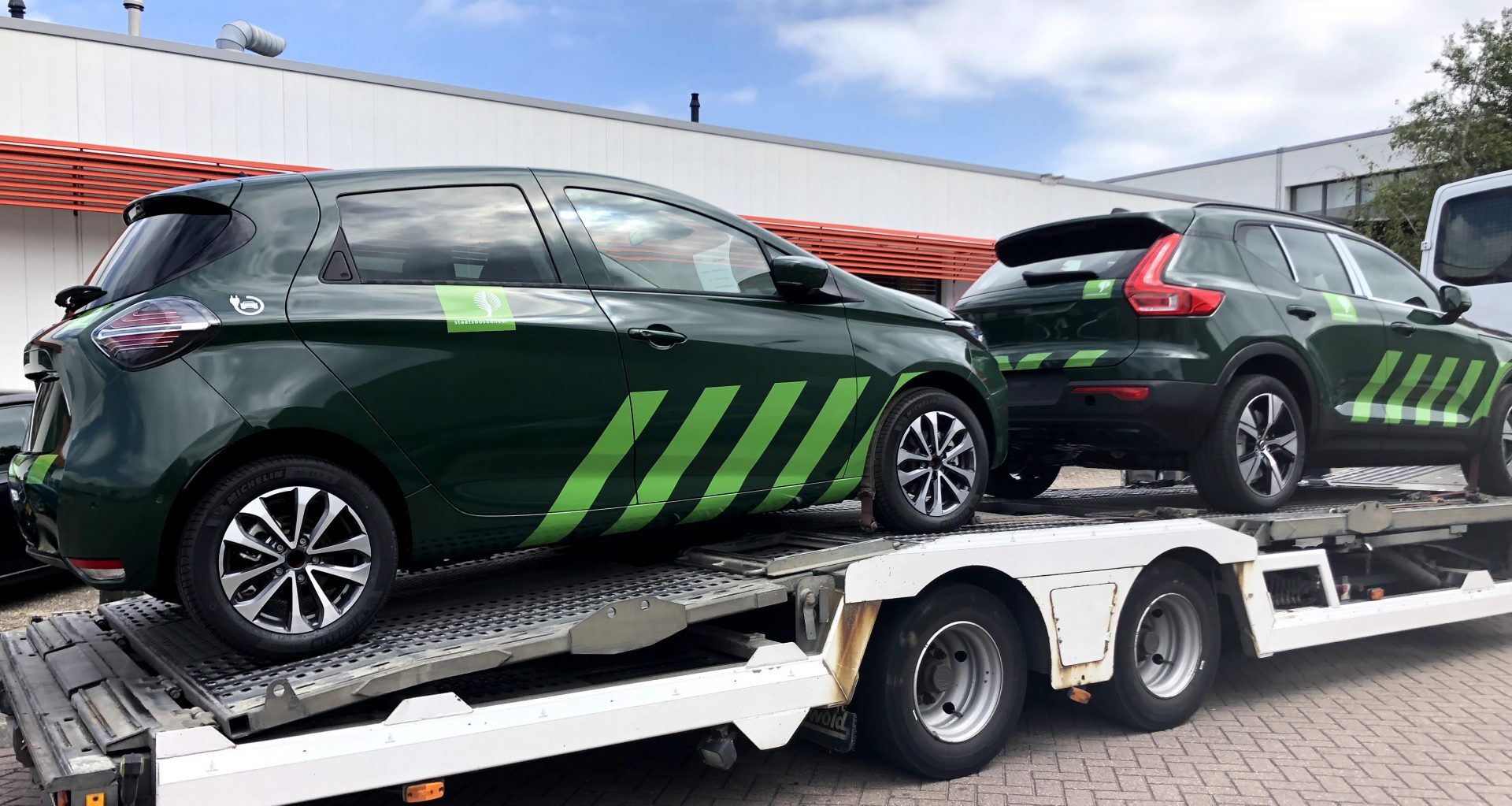 Twee groene prototypes van auto's met diagonale strepen staan op een transporttrailer.