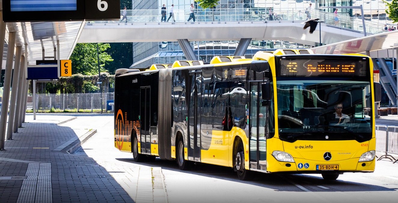 Een gele Qbus-bus stopt bij een bushalte in een stedelijke omgeving.