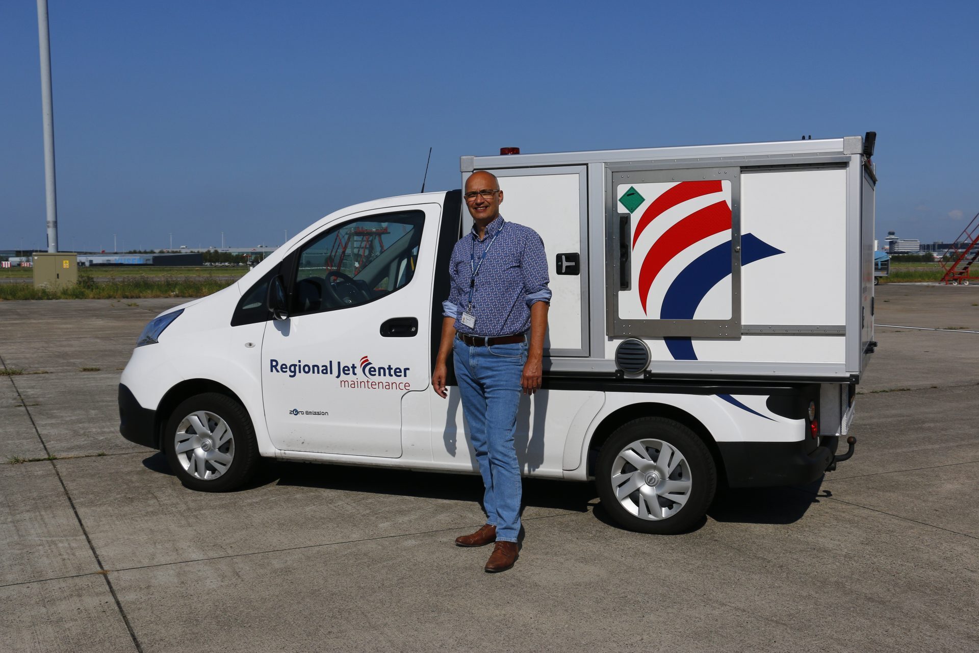 Een man staat naast een bestelwagen van Regional Jet Center Maintenance op een open terrein.
