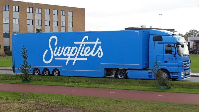 Blauwe vrachtwagen met het logo van Swapfiets op de zijkant, geparkeerd langs de weg.