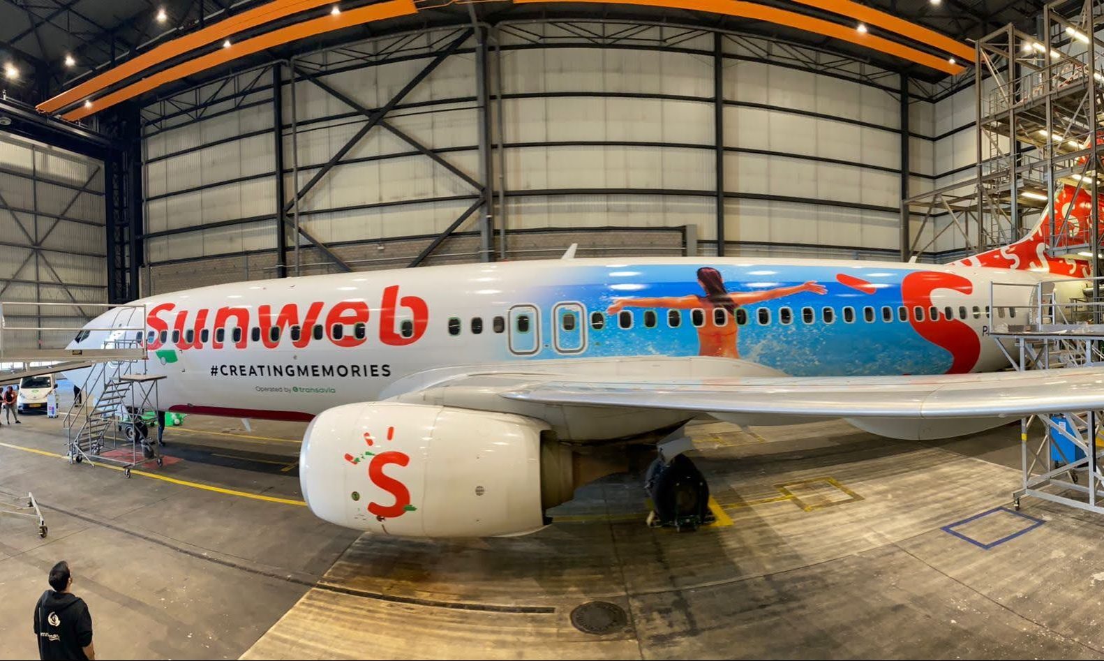 Een vliegtuig met Sunweb-logo en kleurrijke opdruk staat geparkeerd in een hangar.