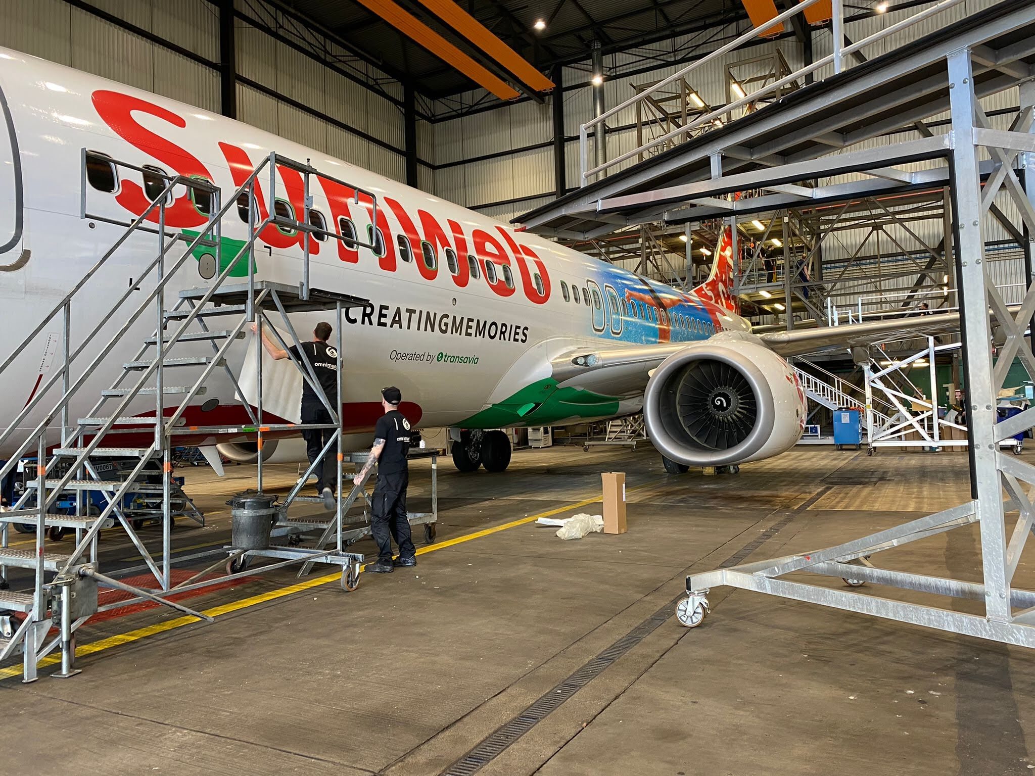 Een Sunweb-vliegtuig wordt onderhouden in een hangar door technici met roltrappen ernaast.