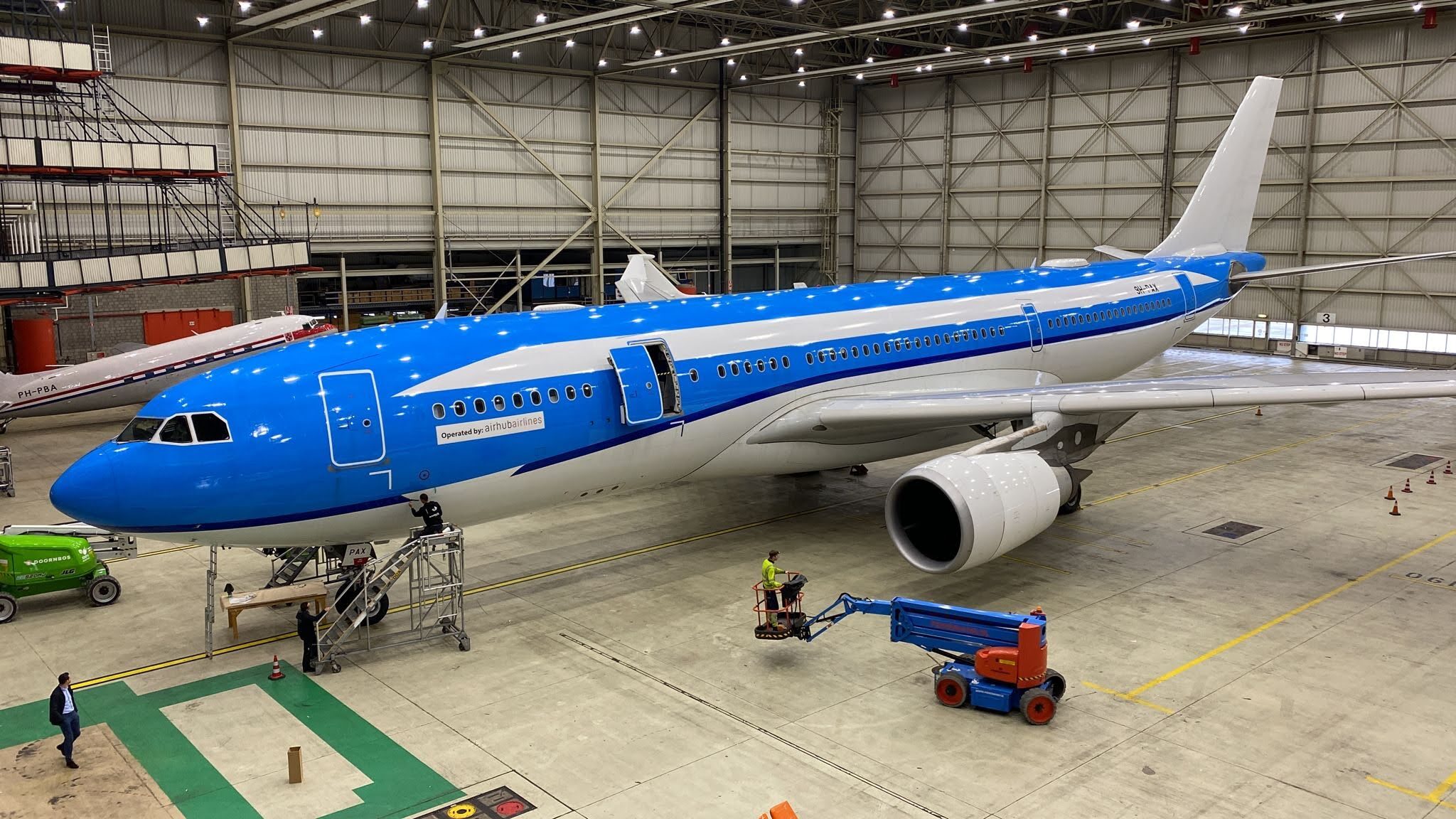 Blauw-en-wit vliegtuig in een hangar met techniekers die onderhoudswerkzaamheden uitvoeren.