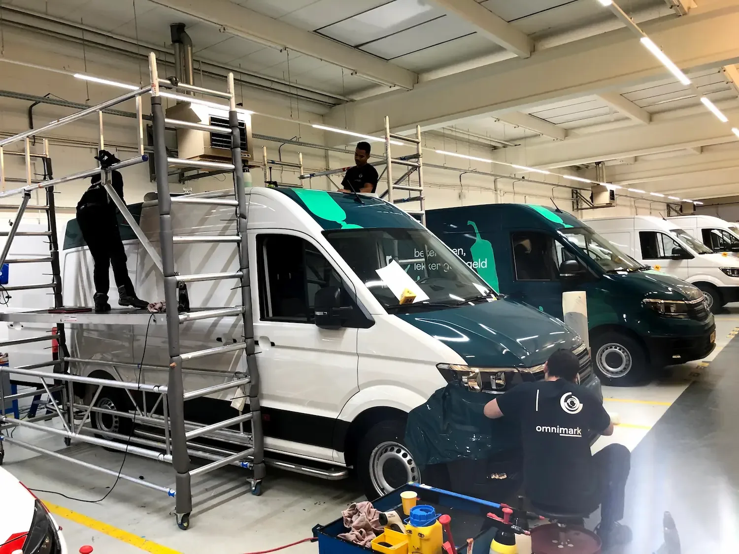 Werknemers beplakken bestelwagens met folie in een werkplaats.