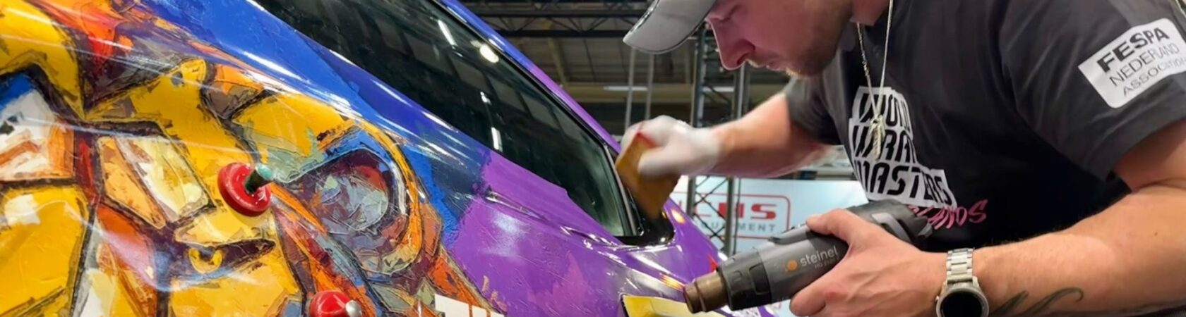Een persoon is een auto aan het wrappen met kleurrijke graphics en de tekst 
