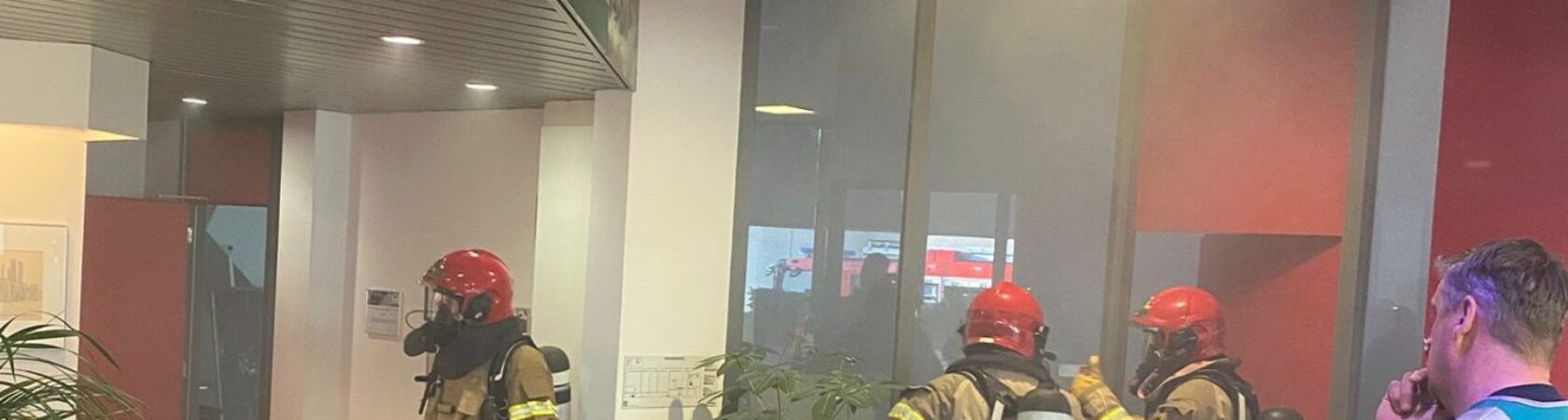 Brandweerlieden met rode helmen en ademhalingsapparatuur werken in een gebouw vol rook.