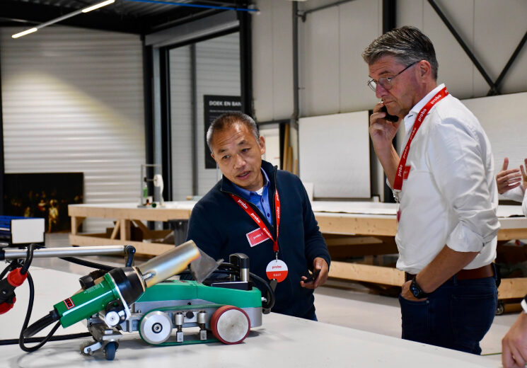 Twee mannen in een industriële ruimte bekijken en bespreken een machine op een werkbank.
