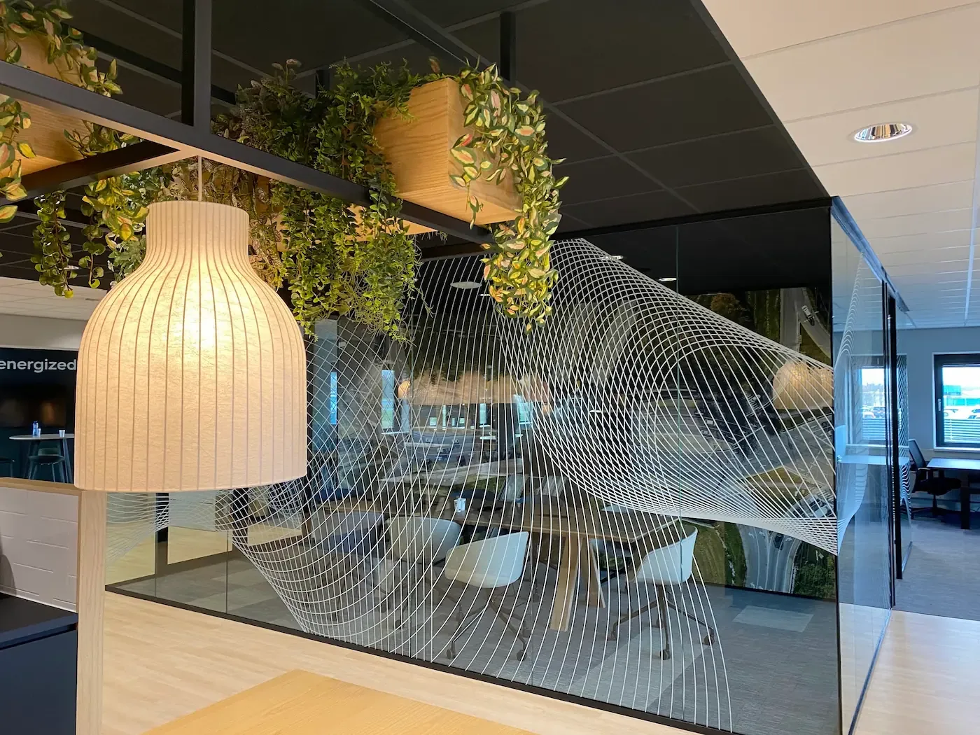 Een modern kantoorinterieur met glazen wanden, hangende planten en een houten lamp.