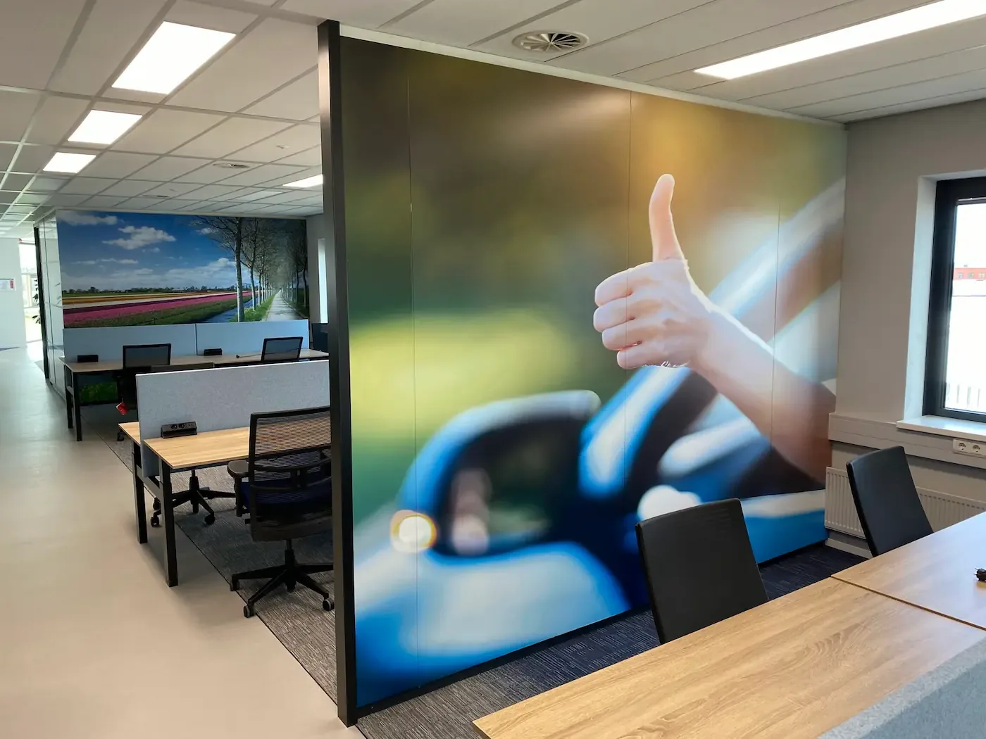 Een moderne kantoorruimte met bureaus, stoelen en een grote muurafbeelding van een duim omhoog.