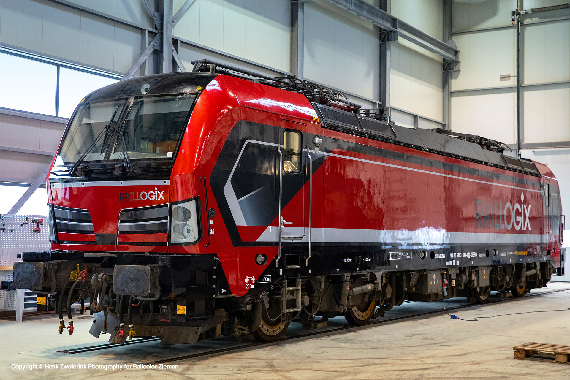 Een rood-zwarte Raillogix locomotief geparkeerd in een moderne onderhoudsloods.
