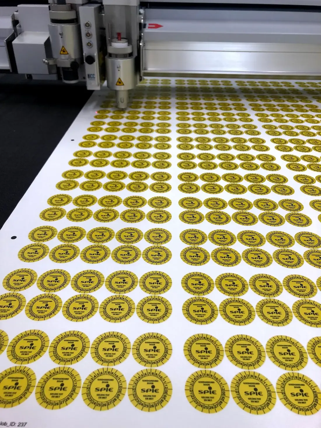 Een vel met gele ronde stickers wordt gesneden door een machine.