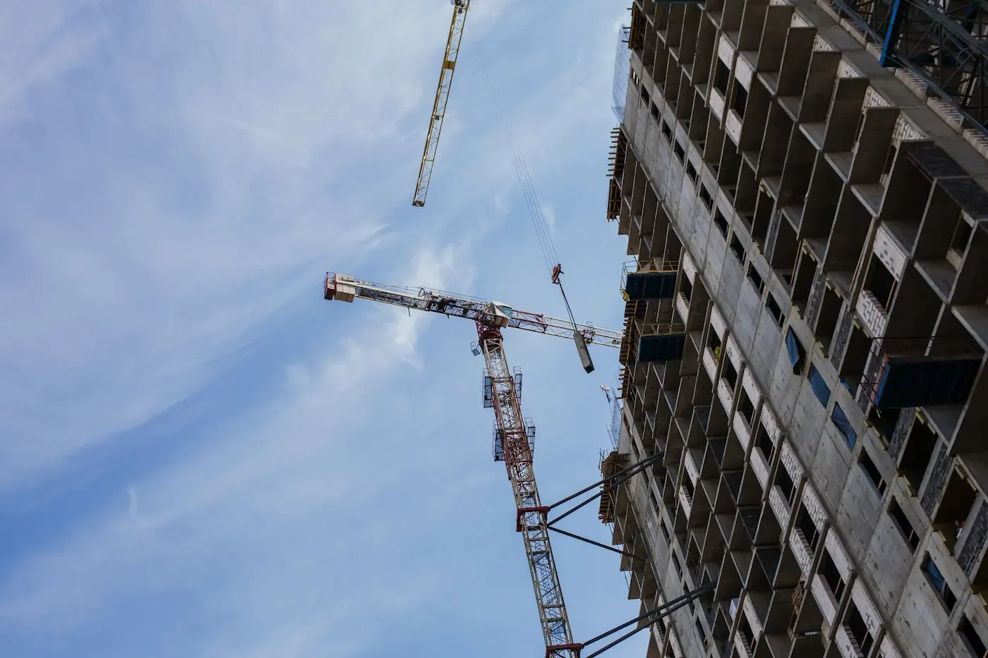 Torenkranen aan het werk tegen een blauwe lucht bij een bouwplaats met onafgewerkte gebouwen.