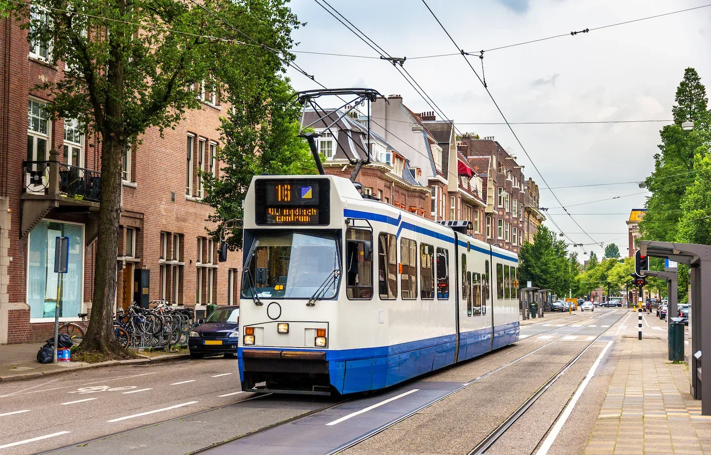 Een tram rijdt door een straat in Amsterdam, Nederland, omringd door bakstenen gebouwen en bomen.