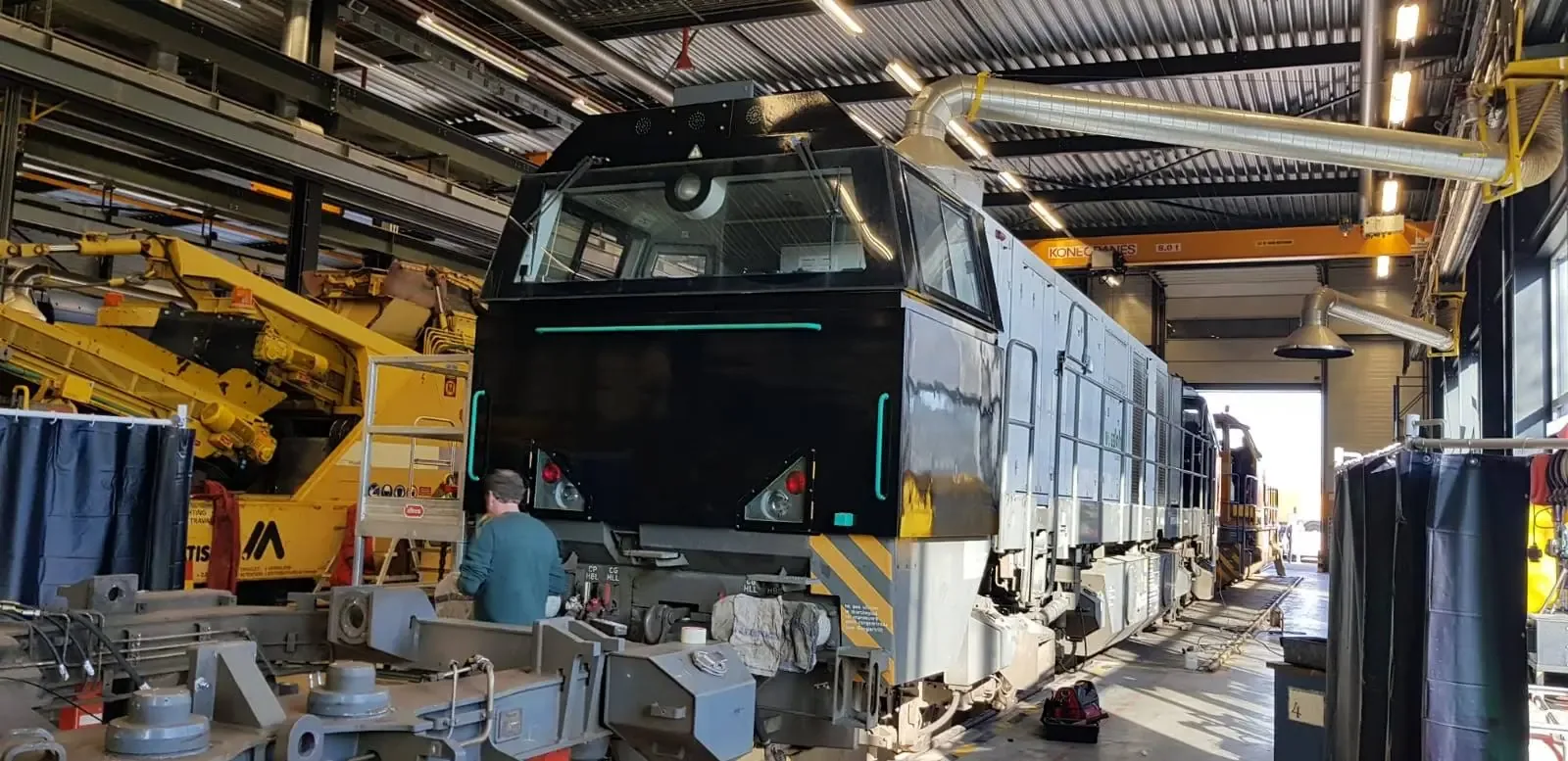 Een zwarte locomotief in een onderhoudsruimte met machines en apparatuur.